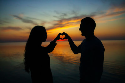 Silhouette woman with arms raised against sky during sunset