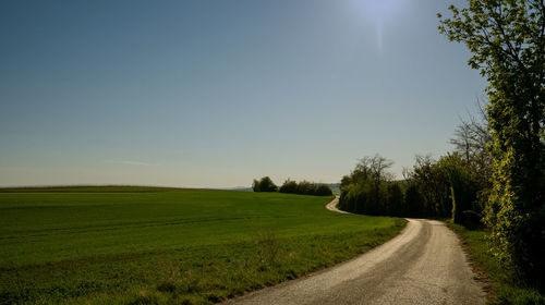 Empty road amidst field against sky
