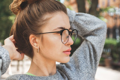 Close-up of young woman looking way with hands behind head in park