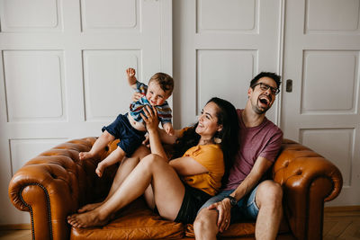 Cheerful father and mother with son on sofa at home