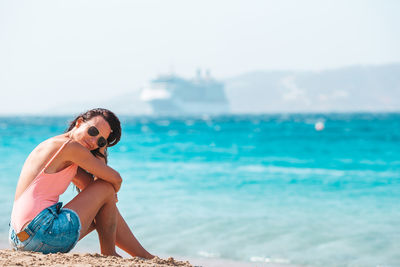 Side view of woman sitting on beach against sky