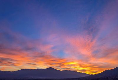 Scenic view of silhouette mountains against dramatic sky during sunset