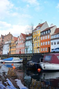 Sailboats moored on canal by buildings in city against sky