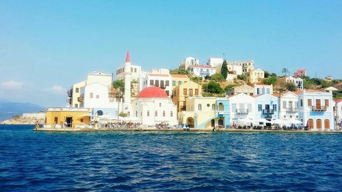 Buildings by sea against clear blue sky