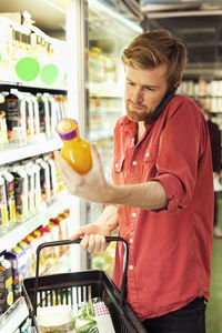 Man answering mobile phone while shopping juice bottle at freezer section in supermarket