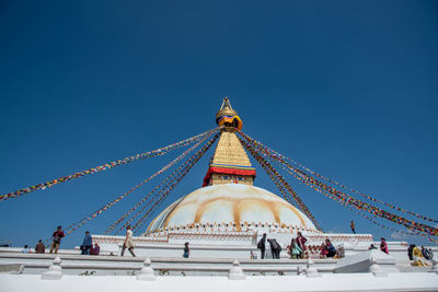 Low angle view of people outside building against clear blue sky