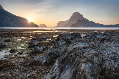 Rock formations at beach against sky during sunset