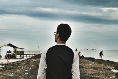 Rear view of man standing at beach against sky