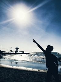 Silhouette person standing by sea against sky on sunny day