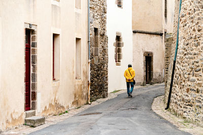 Rear view of man with yellow jacket walking on a street with old buildings.