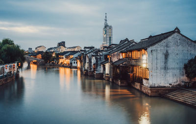 Bridge over river by buildings against sky at dusk