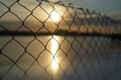 Close-up of chainlink fence against sky during sunset