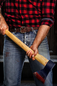 Midsection of lumberjack holding axe outdoors