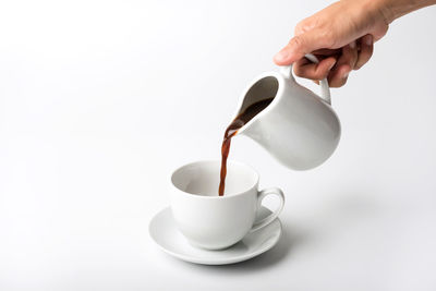 Close-up of hand pouring coffee cup against white background