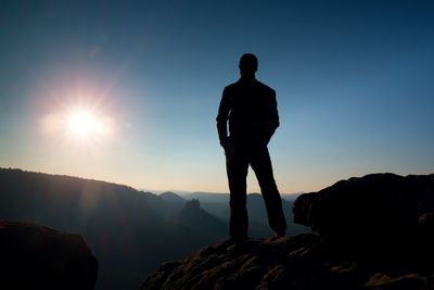 Silhouette man standing on rock against sky