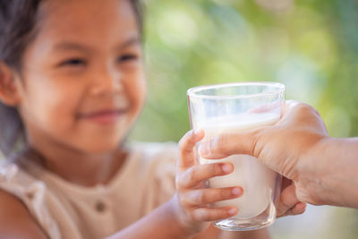 Cropped hand of mother giving milk glass to daughter outdoors