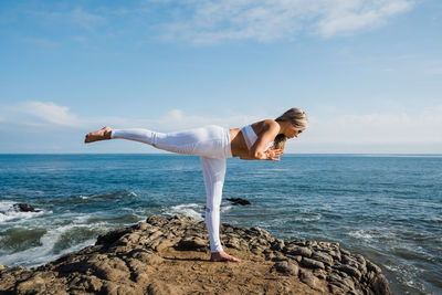 Woman standing on rock by sea against sky