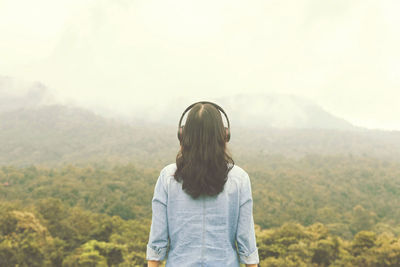 Rear view of woman listening music while standing against mountain range