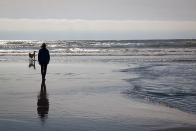 Woman walking on calm beach against sky