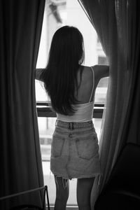 Rear view of woman standing by window