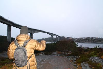 Rear view of man standing by bridge over river against sky