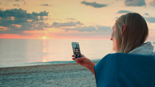 Portrait of woman photographing sea during sunset