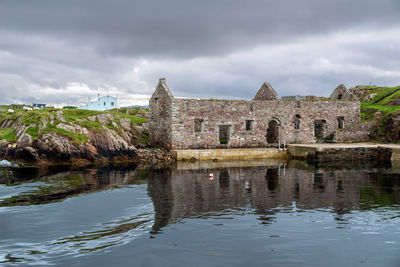 Old building by lake against cloudy sky