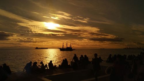 Silhouette people by sea against sky during sunset