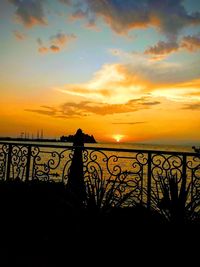 Silhouette railing against sea during sunset