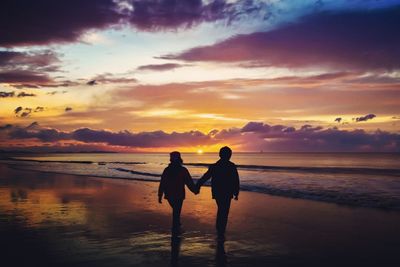 Silhouette friends standing on beach against sky during sunset