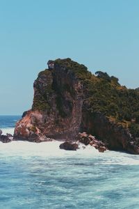 Rock formation in sea against clear blue sky