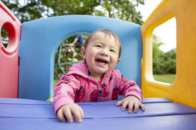 Happy smiling toddler girl plays on colorful jungle gym in backyard