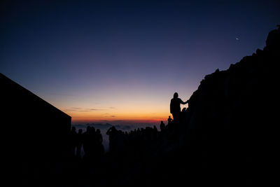 Silhouette people on rock against sky during sunset