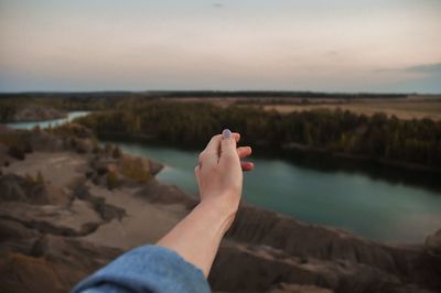 Midsection of person hand by lake against sky