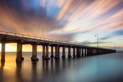 Bridge over sea against dramatic sky at dusk