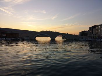 Arch bridge over river against sky during sunset