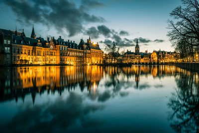 Illuminated buildings by river against sky at dusk