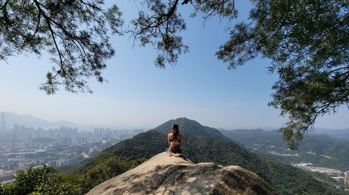 Man sitting on rock against sky