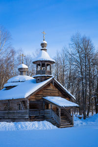 Snow-covered, ancient, wooden church among the trees against the blue sky