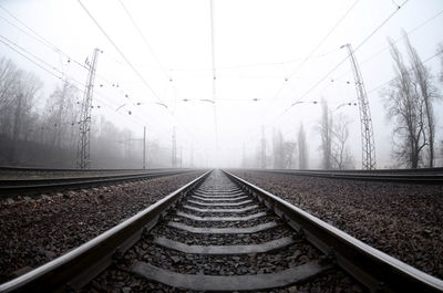 Diminishing perspective of railroad track against sky during foggy weather