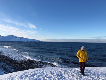 Man standing on snowcapped mountain with sea in background 