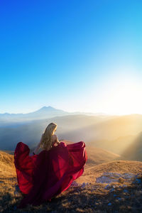 Rear view of woman wearing red dress on mountain against clear blue sky during sunset