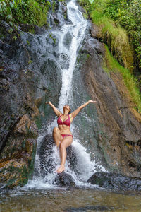 Rear view of shirtless man jumping in waterfall