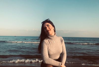 Smiling young woman sitting at beach against sky