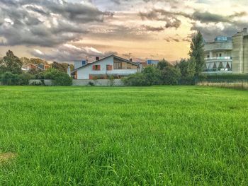 View of grassy field in front of houses against cloudy sky