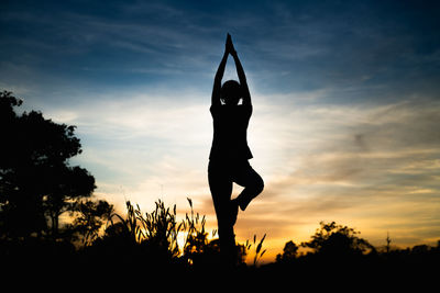 Silhouette man with arms raised against sky during sunset