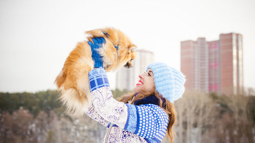 Woman playing with puppy against sky during winter