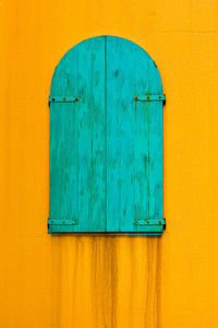 Close-up of turqoise wooden window on yellow wall