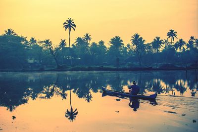 Man in boat sailing in river against sky during sunset