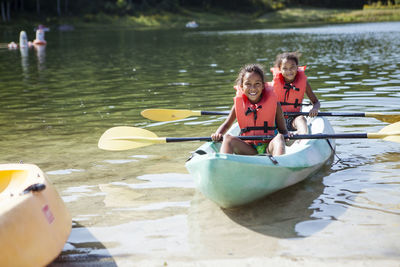 Portrait of friends with oars wearing life jackets while sitting in canoe on lake